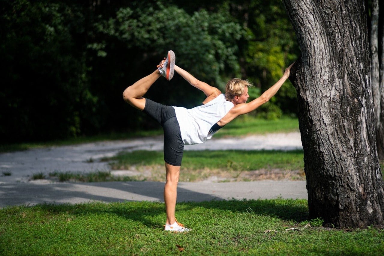 Natalia stretching outdoors beside a tree